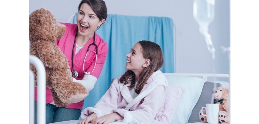 Young nurse in pink uniform holding a teddy bear and having fun with a little patient e learning brothers